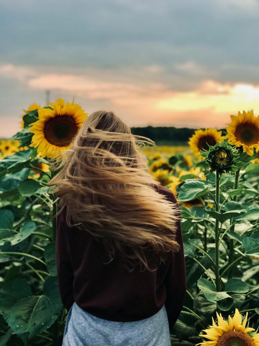 A young woman stands among blooming sunflowers as the sun sets, creating a serene atmosphere.